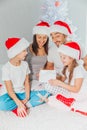 Young mother, father and two little children opening a magical Christmas gift by a Christmas tree in cozy living room in Royalty Free Stock Photo