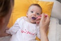 Young mother feeding a baby at home with a spoon. Happy little cute daughter with blue eyes. The baby girl is four months old Royalty Free Stock Photo