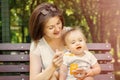 Smiling mother feeding child with pumpkin puree on bench outdoor. Kid does not want to eat, baby is turning face away from spoon Royalty Free Stock Photo