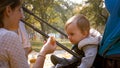 Portrait of young mother feeding her toddler boy sitting in stroller at park Royalty Free Stock Photo