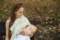 Young mother feeds the baby on a bench in the Park. Mom breastfeeding baby in public place