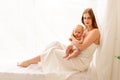 A young mother gently embraces a child in her arms while sitting on the window, the concept of mother`s love and care for the Royalty Free Stock Photo