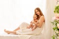 A young mother gently embraces a child in her arms while sitting on the window, the concept of mother`s love and care for the Royalty Free Stock Photo