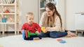 Young mother helping her baby son and playing with him on carpet in lviing room Royalty Free Stock Photo