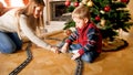 Young mother helping little son building tailways for toy train under Christmas tree at living room. Child receiving Royalty Free Stock Photo