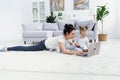 Young mother and her adorable daughter are using laptop while lying on the floor. Royalty Free Stock Photo