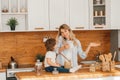 Young mother with her baby daughter in a modern kitchen setting. Young attractive cook woman desperate in stress, tired Royalty Free Stock Photo