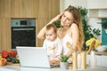 Young mother with her baby daughter in a modern kitchen setting. Young attractive cook woman desperate in stress Royalty Free Stock Photo
