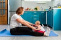 A young mother with her baby is doing yoga on a mat in the kitchen. The concept of home sports training with children Royalty Free Stock Photo