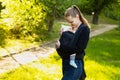 A young mother with her baby in a sling scarf is standing in a sunlight. Mom looks at the child. Wrapping sling for carrying a Royalty Free Stock Photo