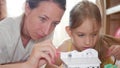 Young mother and her beautiful daughter, paint a paper house, lying on the floor at home, lifestyle, creativity