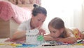 Young mother and her beautiful daughter, paint a paper house, lying on the floor at home, lifestyle, creativity