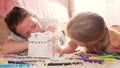 Young mother and her beautiful daughter, paint a paper house, lying on the floor at home, lifestyle, creativity