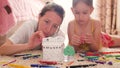 Young mother and her beautiful daughter, paint a paper house, lying on the floor at home, lifestyle, creativity