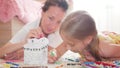 Young mother and her beautiful daughter, paint a paper house, lying on the floor at home, lifestyle, creativity