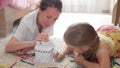 Young mother and her beautiful daughter, paint a paper house, lying on the floor at home, lifestyle, creativity