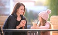 Young mother and her child daughter having good time together sitting at street cafe with hot drinks on sunny fall day Royalty Free Stock Photo