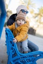 Young mother with her cute infant baby boy child on bench in city park. Royalty Free Stock Photo