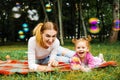 Young mother with her cute little girl is blowing a soap bubbles in summer park. Royalty Free Stock Photo