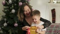 Cute, happy, excited mom and son unwrap a Christmas gift box in a beautiful room.