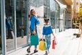 Beautiful mom and her cute little daughter are holding shopping bags, looking at camera and smiling while standing outdoors. Royalty Free Stock Photo