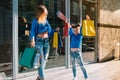 Beautiful mom and her cute little daughter are holding shopping bags, looking at camera and smiling while standing outdoors. Royalty Free Stock Photo