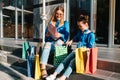 Beautiful mom and her cute little daughter are holding shopping bags, looking at camera and smiling while standing outdoors. Royalty Free Stock Photo