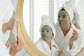 Young mother and her daughter with facial masks having fun near mirror in bathroom Royalty Free Stock Photo