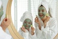 Young mother and her daughter with facial masks near mirror in bathroom Royalty Free Stock Photo