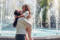 Young mother and her daughter having fun by fountain in summer park. Woman holds girl. Family laughing Royalty Free Stock Photo