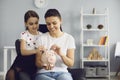 Young mother and her daughter saving money at home, putting coins into piggy bank, space for text. Economic education Royalty Free Stock Photo
