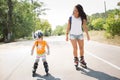 Young mother and her daughter skating on rollers on road alone. Have fun together in sumer. Mother teaches daughter how