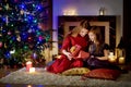 Young mother and her daughter unwrapping Christmas gifts by a fireplace in a cozy dark living room on Christmas Royalty Free Stock Photo
