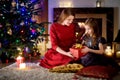 Young mother and her daughter unwrapping Christmas gifts by a fireplace in a cozy dark living room on Christmas Royalty Free Stock Photo