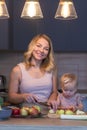 A young mother with her little daughter is cooking in the kitchen. A smiling blonde woman helps her child cut apples. Healthy food Royalty Free Stock Photo