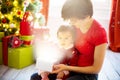 Young mother and her little daughter dressed as santa claus opening a magical Christmas gift by a Christmas tree Royalty Free Stock Photo