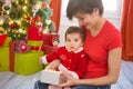 Young mother and her little daughter dressed as santa claus opening a magical Christmas gift by a Christmas tree in cozy Royalty Free Stock Photo