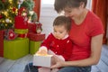 Young mother and her little daughter dressed as santa claus opening a magical Christmas gift by a Christmas tree in cozy Royalty Free Stock Photo