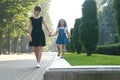 Young mother and her small daughter with long hair walking together holding hands in summer park Royalty Free Stock Photo