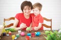 Young mother and her son having fun while painting eggs for Easter. Happy family Mom and children son paint easter eggs with Royalty Free Stock Photo