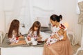 Young mother with her tiny baby sits o the bed with her two daughters dressed in pajamas eating cookies with cocoa with Royalty Free Stock Photo