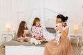 Young mother with her tiny baby sits o the bed with her two daughters dressed in pajamas eating cookies with cocoa with Royalty Free Stock Photo