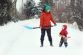 Young mother and her toddler son stand with snow shovels on rural road. Winter seasonal concept