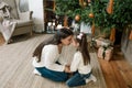 a young mother with her young daughter is sitting under a Christmas tree hugging each other, head in head. happy family Royalty Free Stock Photo