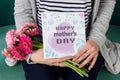 Young mother holding bouquet of gerbera daisies and mother`s day greeting card sitting on a couch. Royalty Free Stock Photo