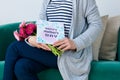 Young mother holding bouquet of gerbera daisies and mother`s day greeting card sitting on a couch. Royalty Free Stock Photo