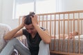 Mother holding head in hands suffering postnatal depression sitting next to baby sleeping in bed Royalty Free Stock Photo