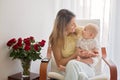 Young mother holding her baby boy, playing with him, sitting in