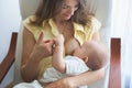 Young mother holding her baby boy, brestfeeding him, sitting in