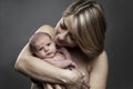 A young mother holds a newborn baby 1 week old in her arms. Love and tenderness in breastfeeding. Close-up. Gray background,